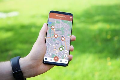 Ein Smartphone wird über einer grünen Wiese in der Hand gehalten. Das Smartphone zeigt eine Übersichtskarte.
